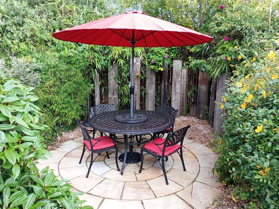 A black iron table and chairs with a lovely red parasol and cushions kept in the garden shed. It sits on a new round patio.  Perfect for summer evenin