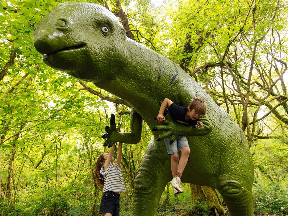 Two children hanging off a huge Dinosaur on the Dinosaur Trail