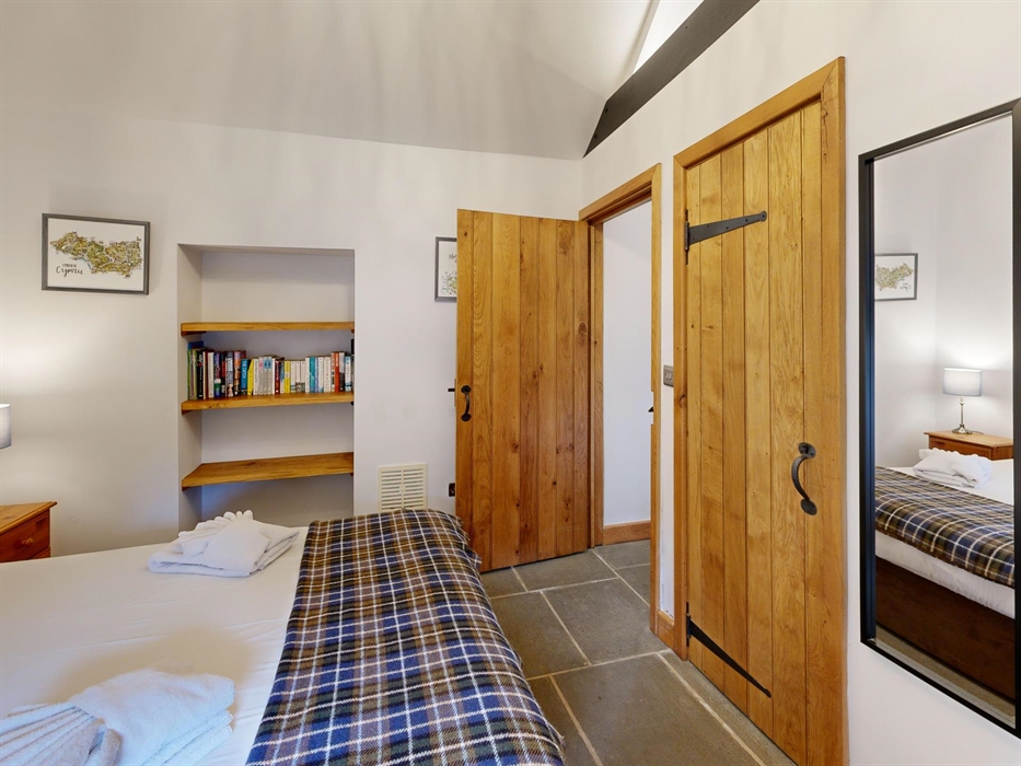 A cosy double bedroom with a check throw, wooden doors, a built-in bookshelf, and bedside lamps