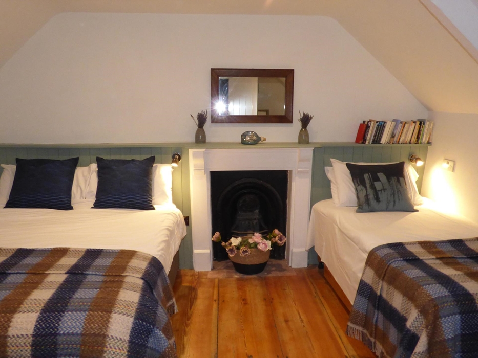 Bedroom at Yr Hal with a double bed and a single. Original wooden flooring and fire place.