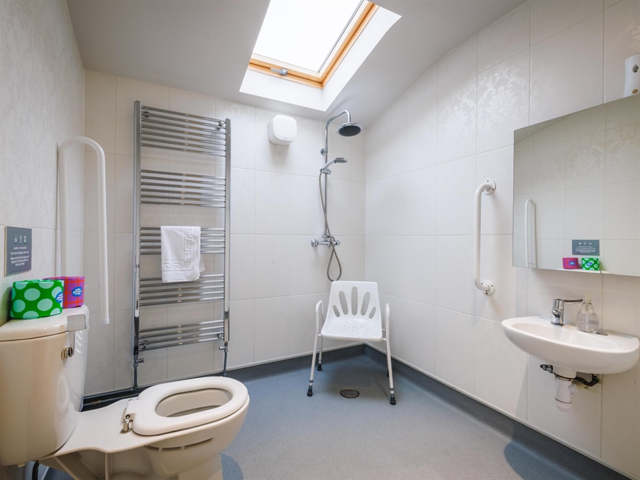 Wet room with shower and accessible chair, hand rails, toilet and sink.