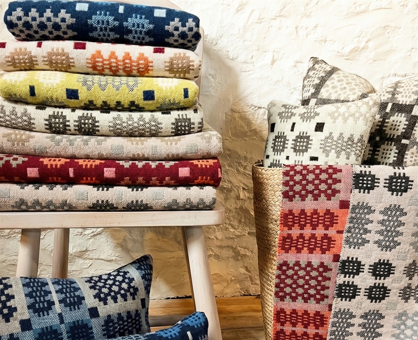 Woven blankets and cushions on display next to a white stone wall.
