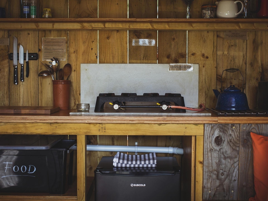 A campfire kitchen with a gas hob, kettle, chefs knives, tea making equipment, a fridge and tea towels.