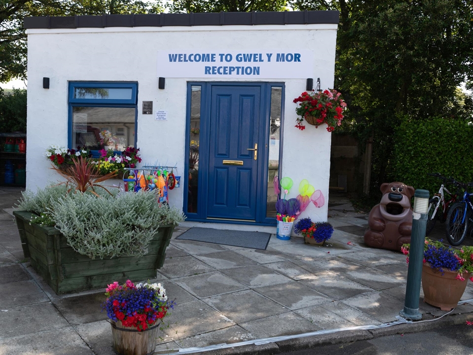 White and blue building of the Reception and shop surrounded by flowers
