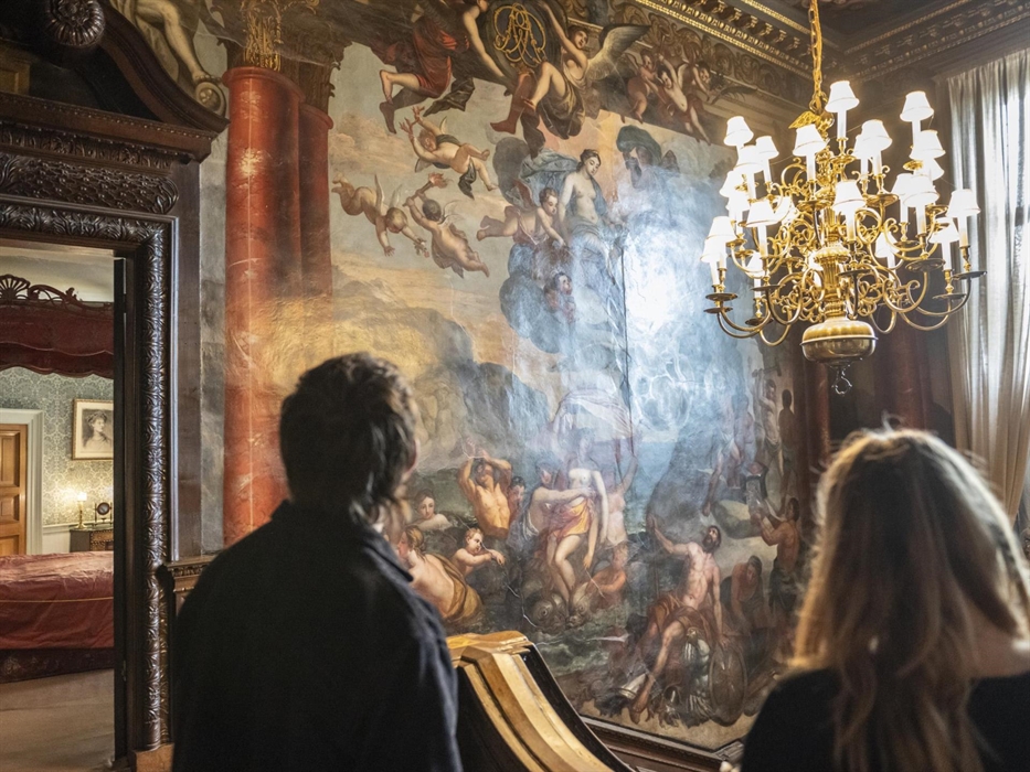 Visitors looking at the walls of the grand staircase which is covered in intricate paintings