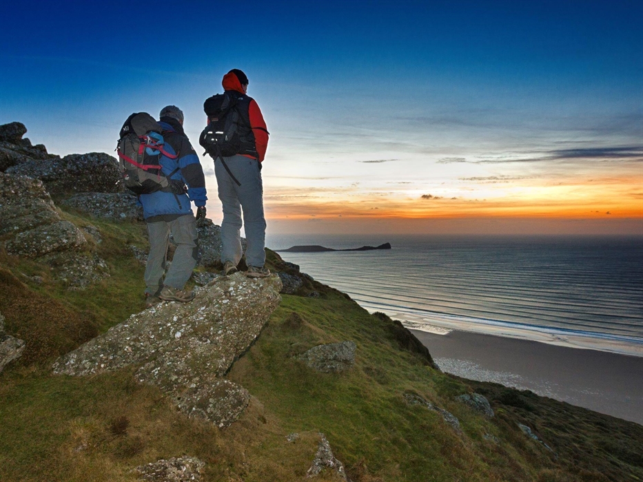 Two male walkers on Rhossili Down at sunset with Worm's Head in background