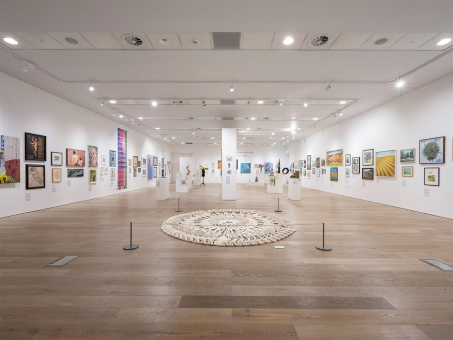 Wide view of the main gallery at Tŷ Pawb, with dozens of artworks hanging on the walls and various sculptures down the middle.