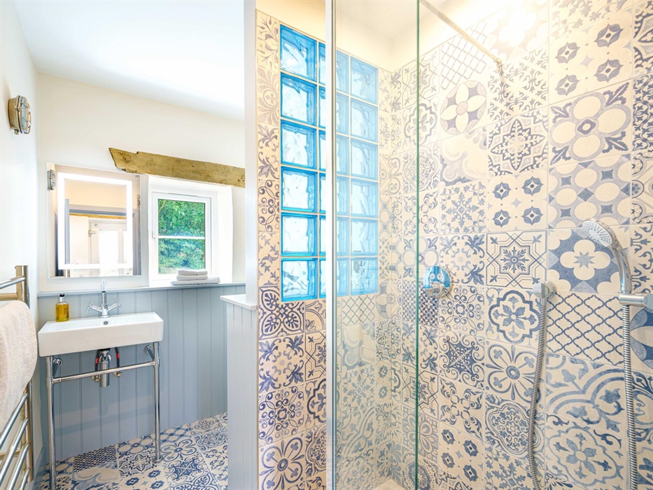 Blue and white tiles adorn this pretty shower room.  Walk in spacious shower. Belfast sink with frame and hot towel rail.   Tongue and groove panellin