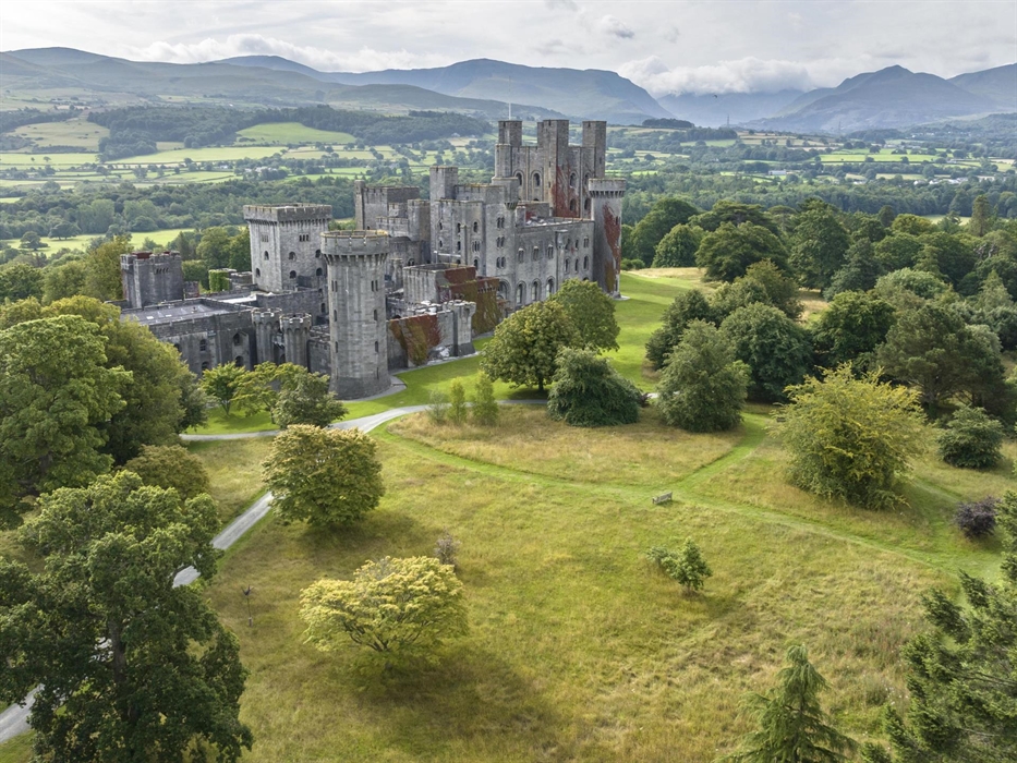 An aerial image of Penrhyn Castle surrounded by meadows with Eryri (Snowdonia) mountain range in the background.