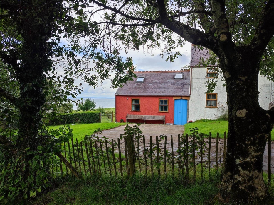 A view through the front garden trees at Ceiliog Bach with sea views to the rear