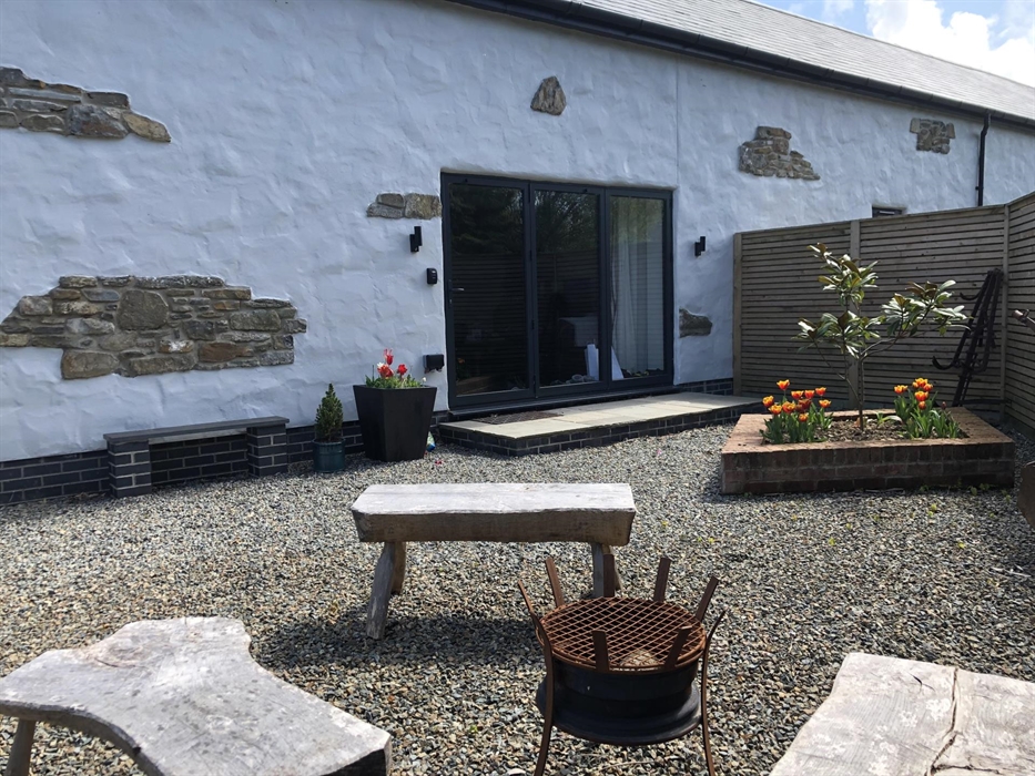 Fire bowl and seats on the front patio. Planter with Magnolia Tree and tulips. Entrance to the property via folding patio doors.