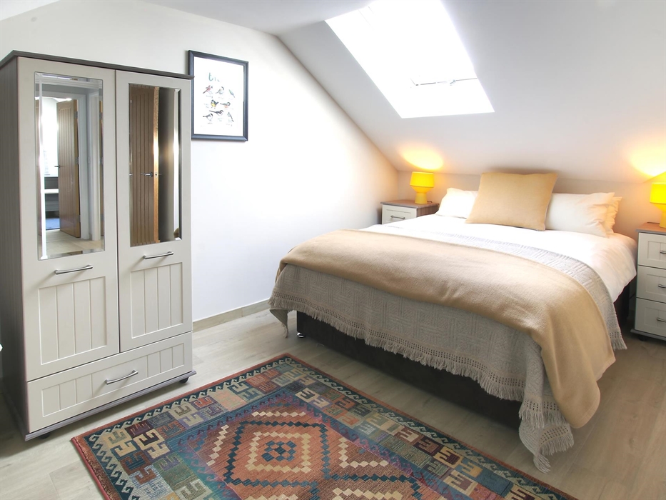 Inviting double bedroom with soft beige tones, mirrored wardrobe, and natural light from the skylight.