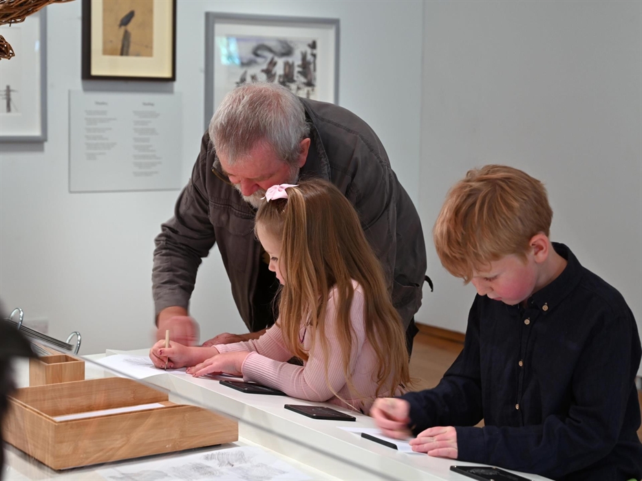 Man and 2 children (boy and girl) doing the rubbings activity at 'The Lost Words' exhibition
