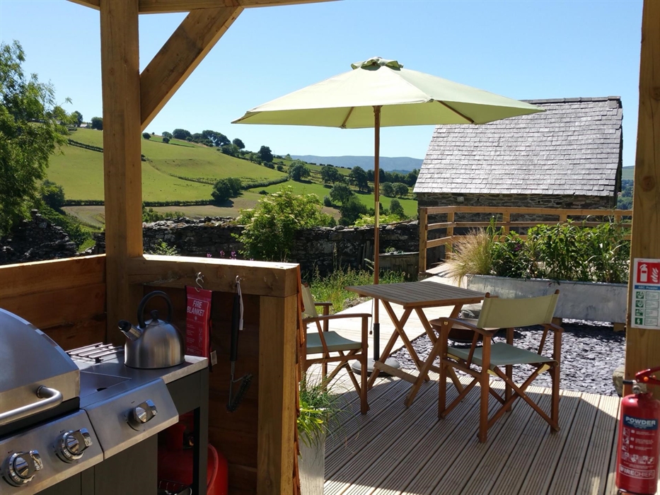 The BBQ and hob in Star's outdoor kitchen with a table and chairs under a parasol and a beautiful view of the hills in the background.