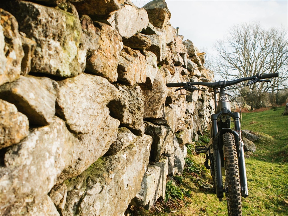 Electric mountain bike propped against a dry stone wall.