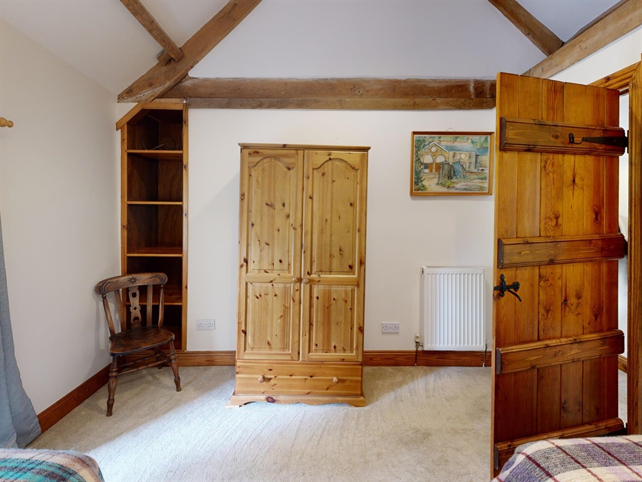 A twin bedroom with warm wood finishes and large sash window overlooking the countryside, blending rustic charm with comfort.