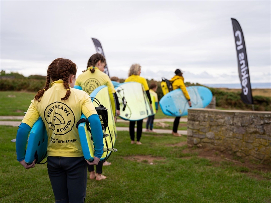 Image of students and their instructor carrying surf boards as they head towards their lesson location