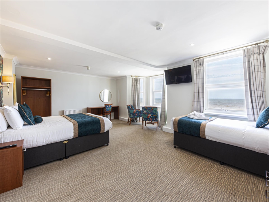 Image shows a triple room, with a double bed on the left and a single bed on the right. Two windows show the view out over the Irish Sea.