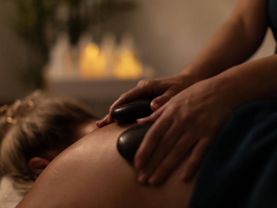 Image shows a guest receiving a relaxing hot stone spa treatment in a dimmed room, lit with candles.
