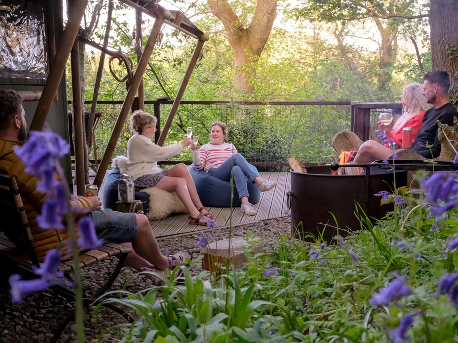 Group of friends around a firepit on the deck of safari tent in the woods at Hay-on-Wye, Wales.  Bluebells
