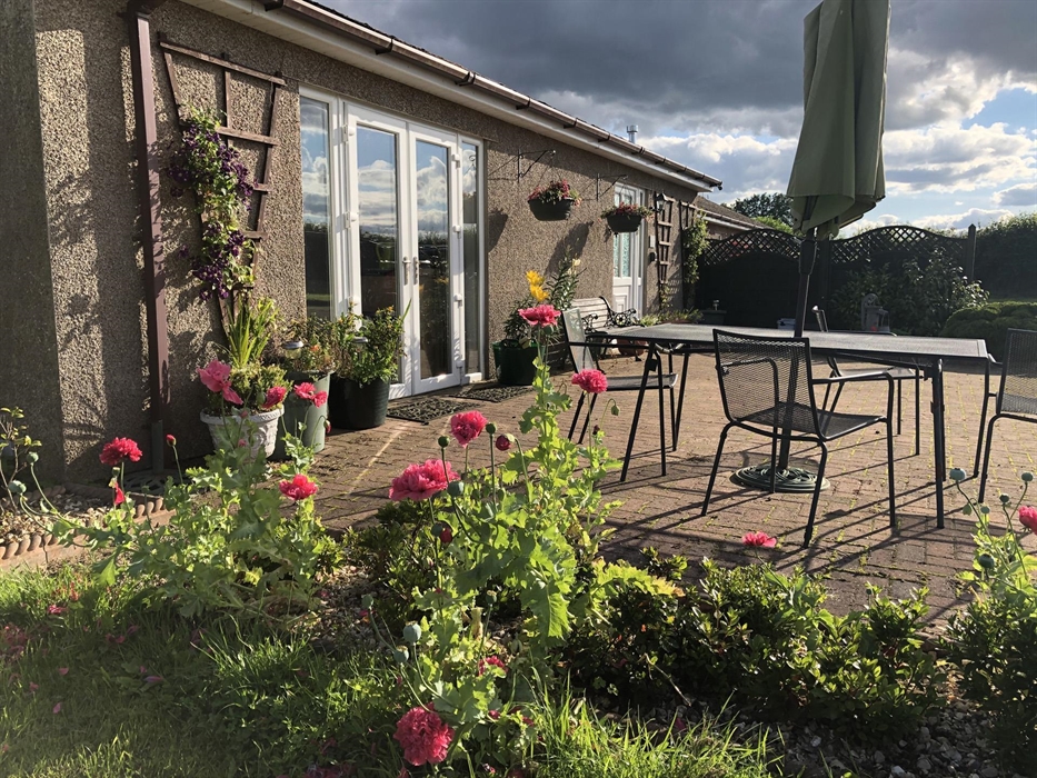 Front view of Blackthorn Lodge showing the lounge patio doors, front door and patio garden area with garden furniture including a table, 4 chairs, par