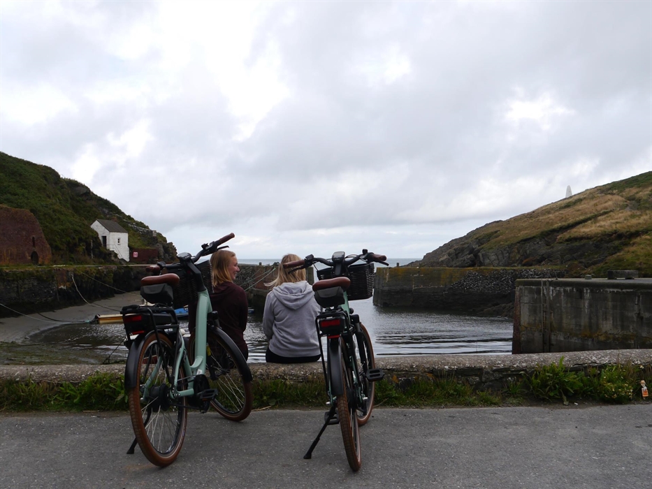 Two women sat at harbour with their e-bikes behind them.