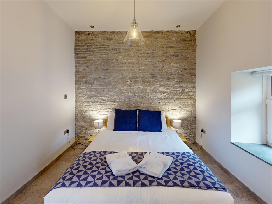 A double bed with deep blue cushions and a geometric throw, set against a rustic stone wall in a peaceful bedroom.