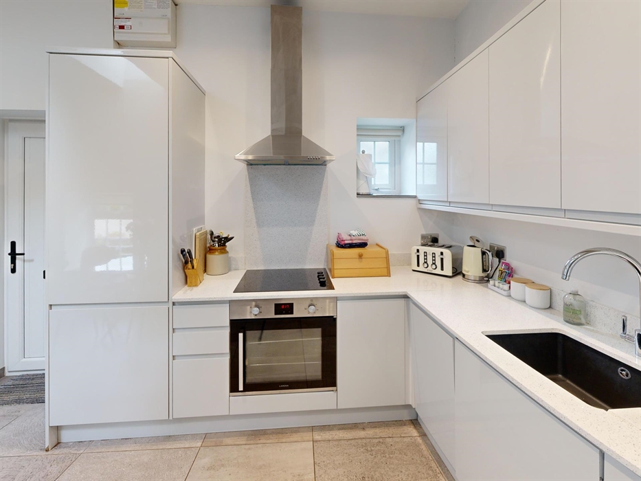 A modern, white gloss kitchen with integrated appliances, hob, and sleek worktops.
