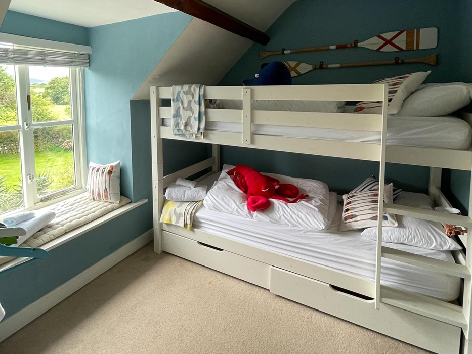 a bunk room with white beds and a soft toy lobster and blue whale with mustard and gray oar cushions and painted oars on the wall