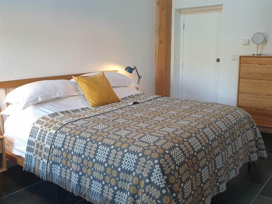 Oak superking bed made up with crisp white linen and a contemporary Welsh blanket in pale grey and yellow.