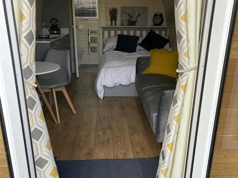 showing inside of pod from door, made up bed, kitchenette, sofa and bathroom