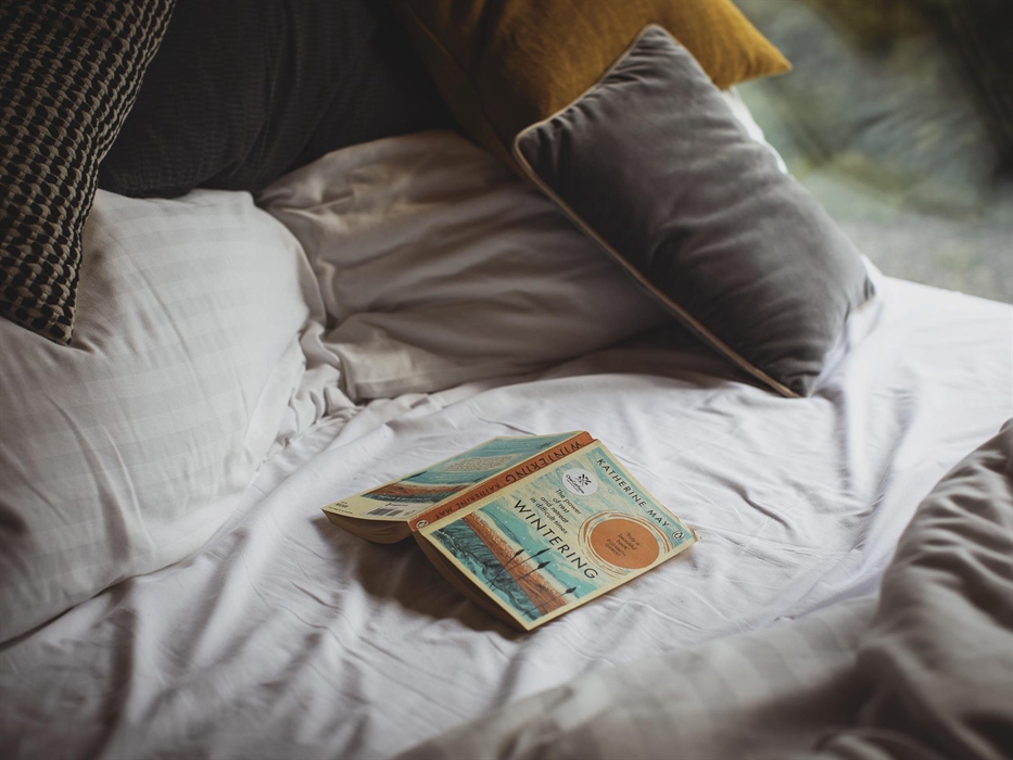 Close up of an unmade bed with an open book on it.
