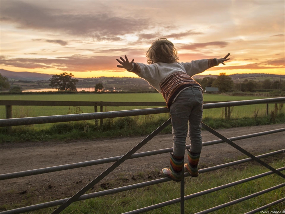 Child on a fence pretending to fly at Llangorse Lake in the Brecon Beacons National Park, Wales