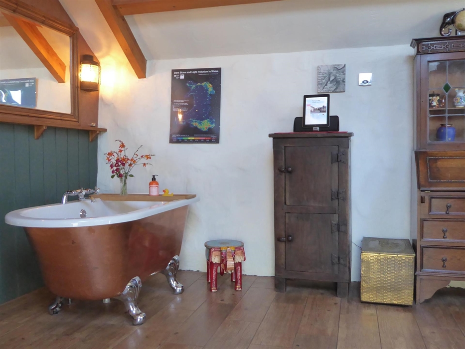 Free-standing roll-top bath and a Indian Elephant on the floor. To right is a bookcase and writing writing bureau.
