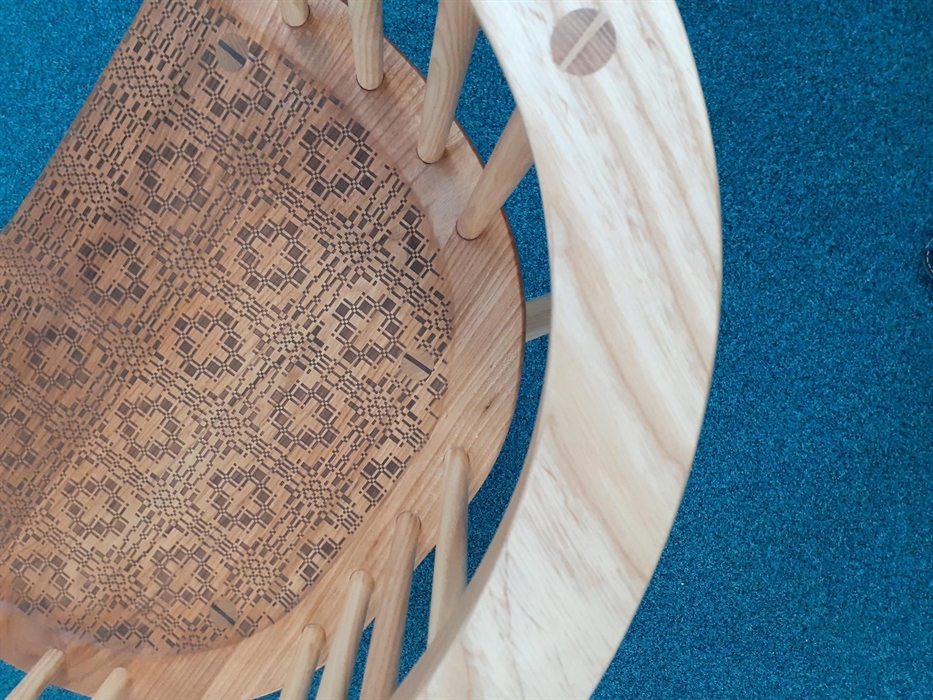 Aerial view looking down on to a wooden chair. The curved arm of the chair can be seen above a number of dowel features leading down to a highly patte