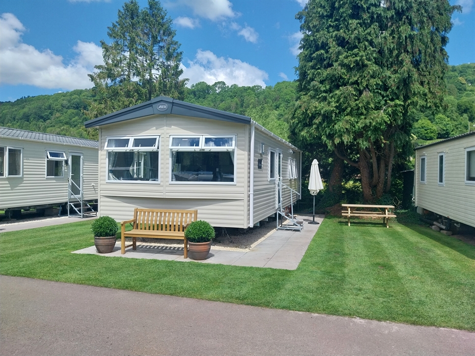 Static caravan with stone slab surround for steps and seating and grass parking area alongside