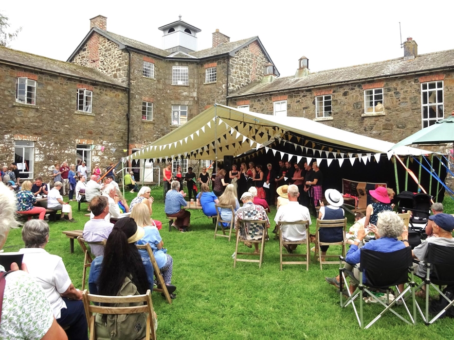 The Vivace Choir performing under a canopy in the Women's Yard at Llanfyllin Workhouse, with an audience sitting on chairs on the lawn.