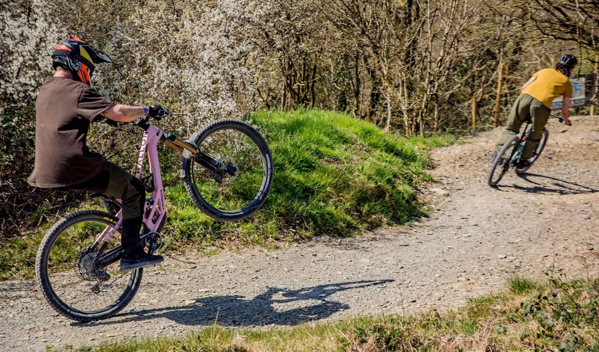 Two riders having fun in the sun, one is pulling a wheelie.
