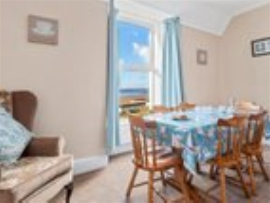 A photograph across the dinning room in apartment 2 showing the table laid and the view of the beach from the dinning room window.