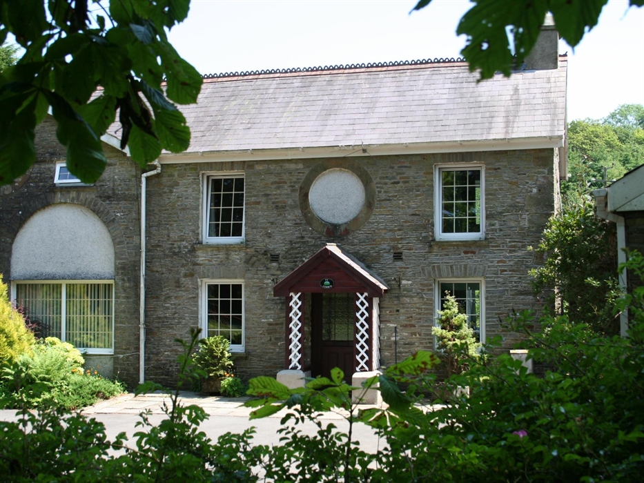 A charming view of Ty Cerbyd’s traditional stone facade with symmetrical sash windows and a decorative circular feature above the door, surrounded by