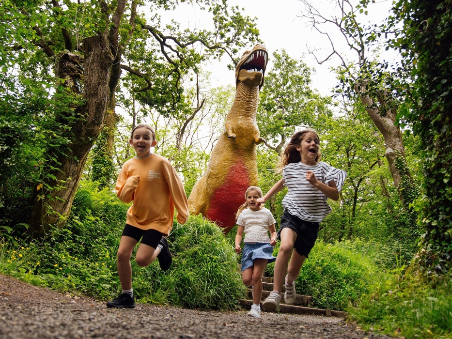 Three girls running away from a huge T-Rex statue on the Dinosaur Trail