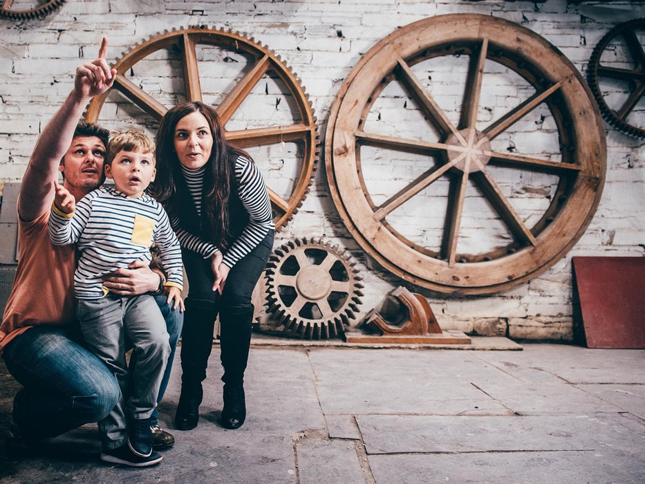 two parents and young son explore the pattern loft. There are wooden models, known as patterns, of wheels and cogs. These patterns were used to cast w