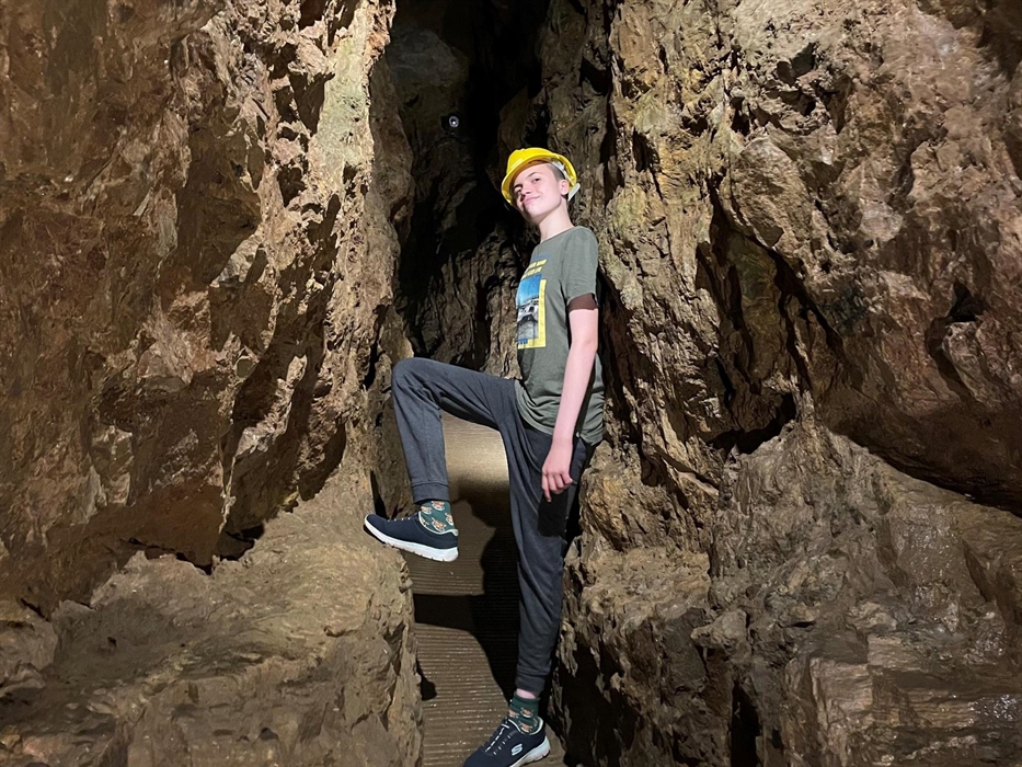 A young teen standing in a narrow section of the underground passageway, just a little wider than shoulder width, he is leaning his back against the r