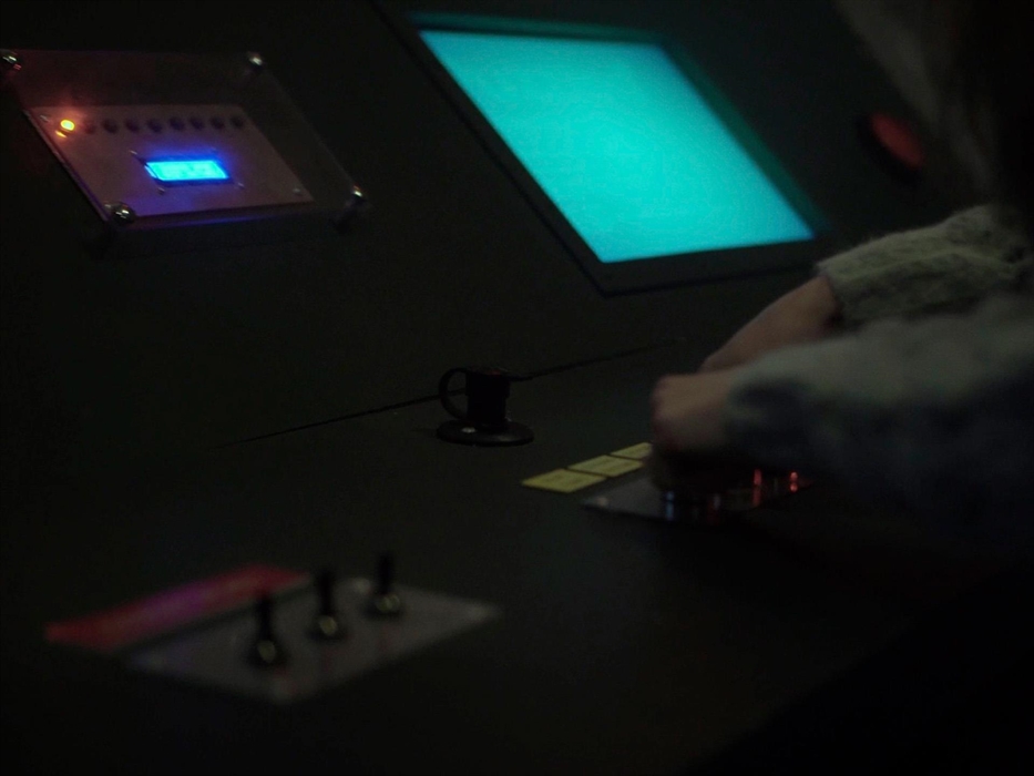 A panel with a red light is pictured above several knobs and switches being played with in an escape room setting.