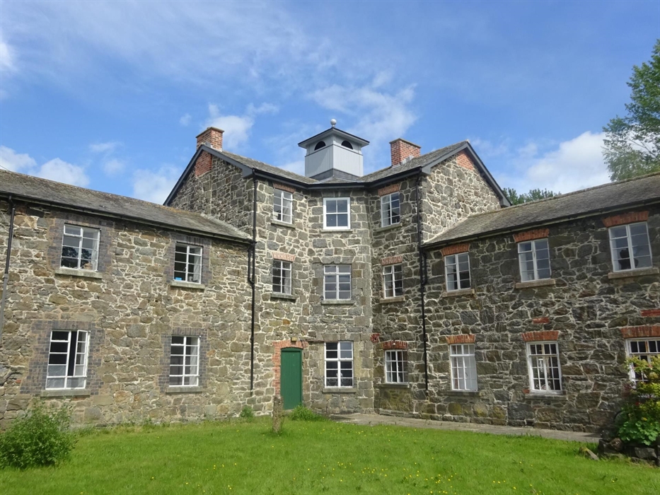 A three-storey building with an octagonal core and a classical cupola, flamked by two-storey wings and built of stone.