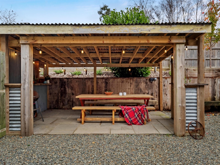 large wooden table with bench seating, charcoal BBQ with tools, lighting and power socket