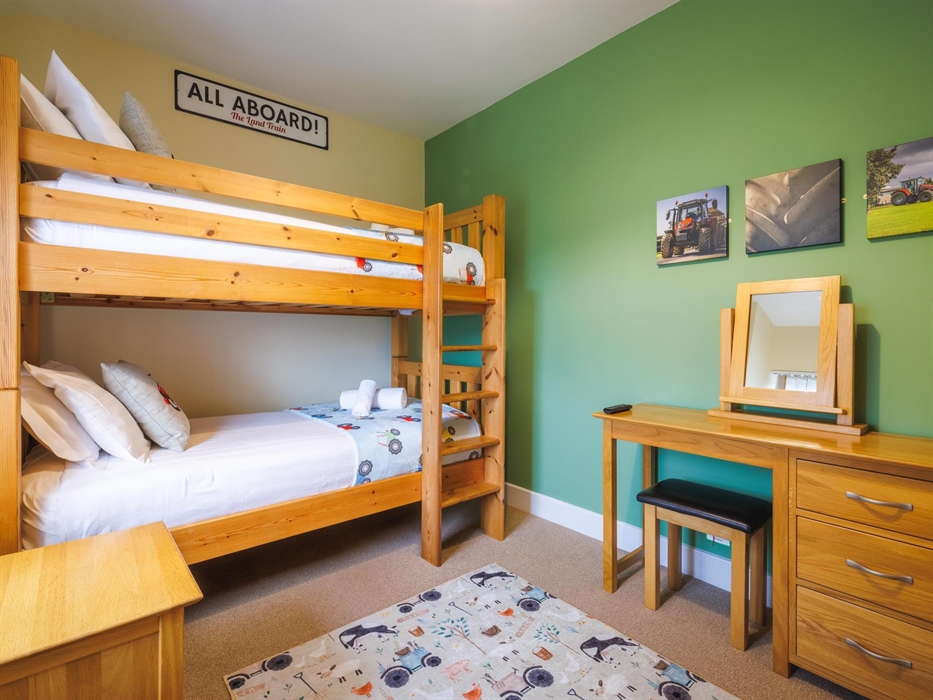 Full size single bunk bed with side table, dressing table and tractor-themed soft furnishings and tractor canvasses on wall.