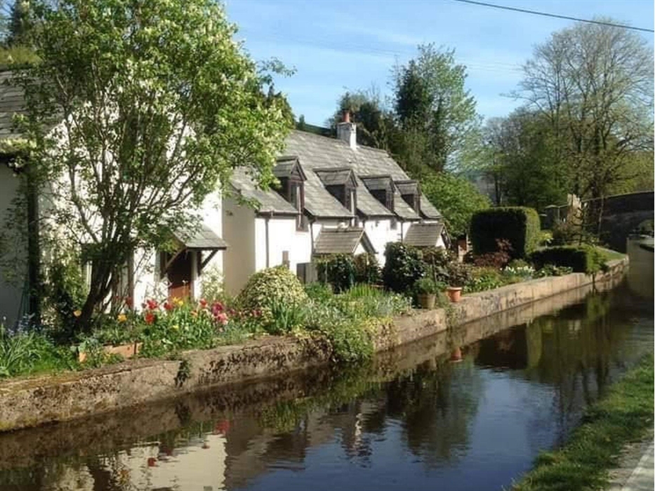 Canal side scenic view as the horse drawn boat travels a long the Llangollen canal edged by trees, foilage and flowers surrounding the canal side cott