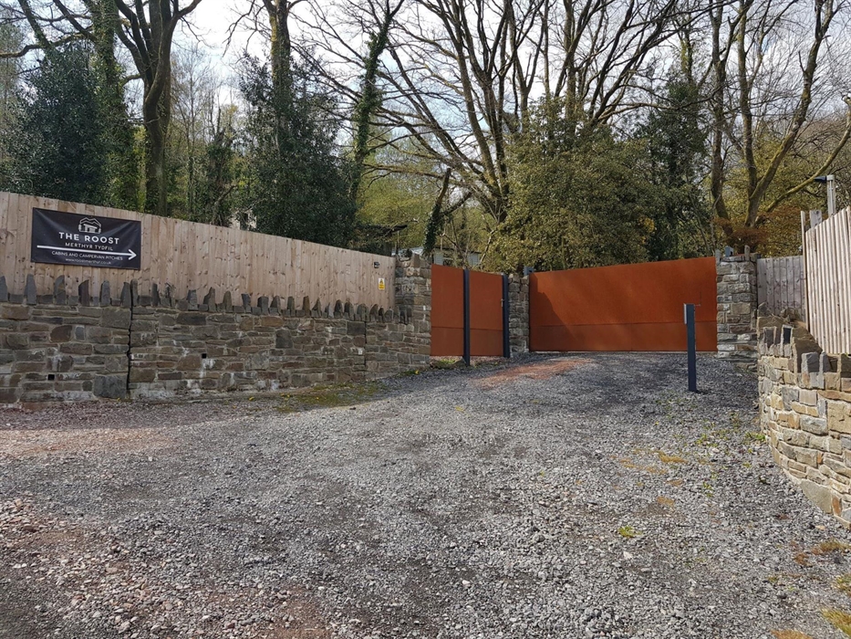 a gravel drive way with stone walls and fence on both signs. There are two gates with an intercom and a sign for the roost.