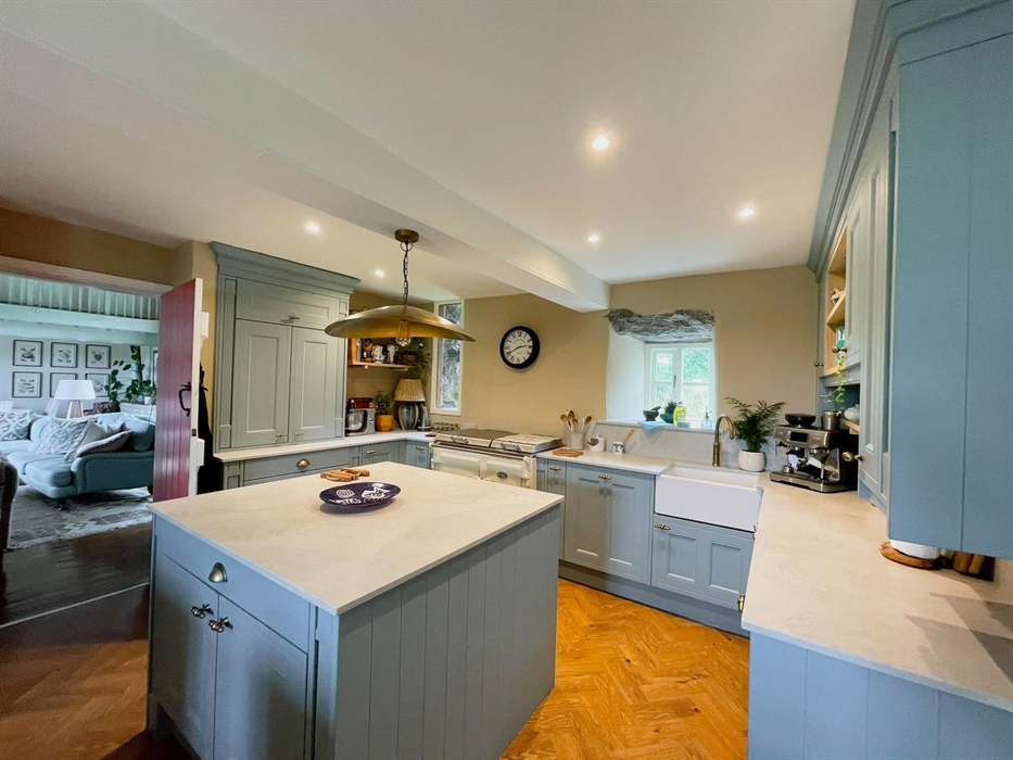 The kitchen at Ysgubor Degwm self catering holiday let near Pwllheli in North Wales. Pale blue units with cement style work tops and brass light.
